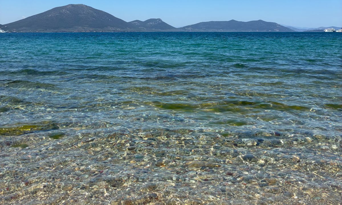 Clear shallow water over pebbles, mountains across the bay