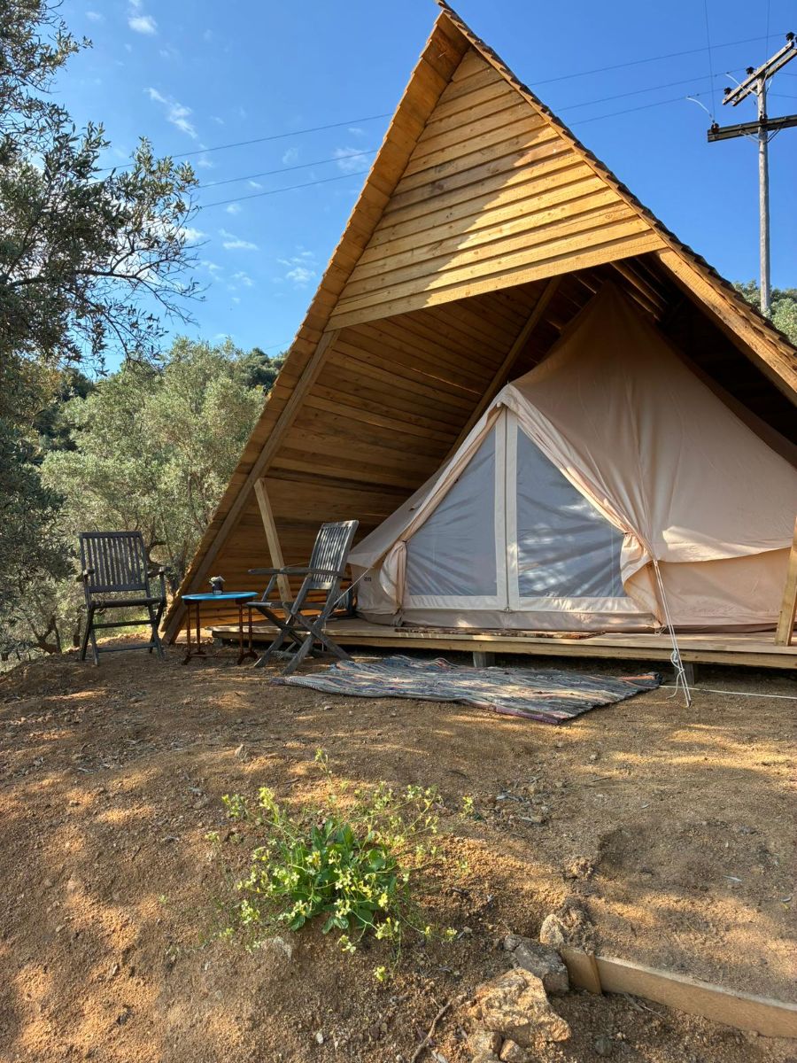 A glamping tipi under its timber shelter, chairs and a rug outside